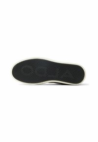 Suela de zapato de goma negra con un patrón texturizado y un logo grabado. Un borde de color crema rodea la suela, destacando su forma y diseño.