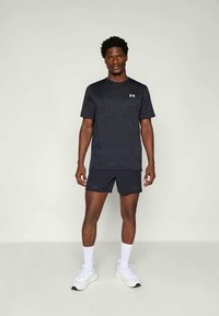 Zwarte sport T-shirt met korte mouwen, gecombineerd met donkere shorts. Bevat een subtiel patroon en een klein wit logo op de borst.