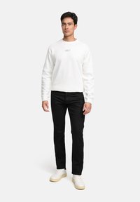 Felpa bianca con collo a giro e stampa minimale, abbinata a pantaloni neri e scarpe bianche. Texture semplice e design casual.