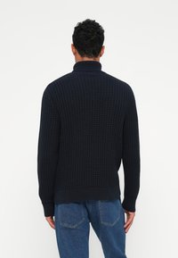 Pull en maille bleu marine avec col haut, motif texturé et poignets côtelés. Le design présente une coupe décontractée et une couleur unie.