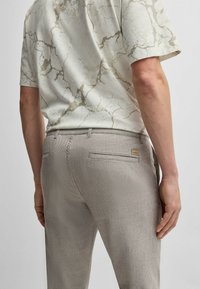 Ljusgrå, strukturerade byxor med två bakfickor och en liten logotags; parat med en kortärmad, krämfärgad skjorta med marmor-mönster.