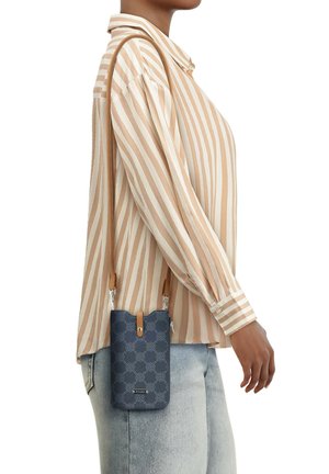 Kreuzbody-Tasche mit Marine-Muster und braunem Ledertrageriemen; rechteckige Form, Reißverschlussverschluss und markante Präge-Details, präsentiert an einem Modell in einem gestreiften Hemd.