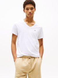 Weisses Baumwoll-V-Ausschnitt-T-Shirt mit kleinem Logo auf der Brust, kombiniert mit beigen Sweatpants mit Kordelzug und seitlichen Taschen.