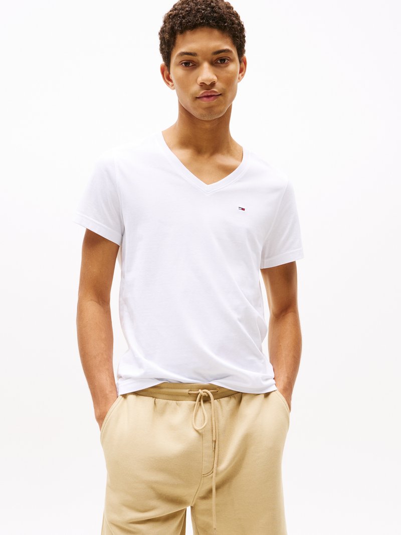 Weisses Baumwoll-V-Ausschnitt-T-Shirt mit kleinem Logo auf der Brust, kombiniert mit beigen Sweatpants mit Kordelzug und seitlichen Taschen.