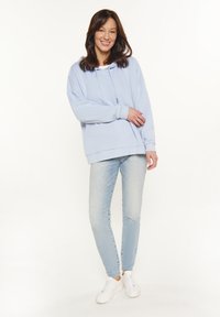 Felpa con cappuccio azzurra chiara realizzata in tessuto morbido, dotata di tasca frontale e lacci, abbinata a jeans skinny chiari e sneakers bianche.