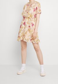 Kukkamekko lyhyillä hihoilla, vaaleanpunaista kangasta, röyhelöhelma ja vyötäröllä vyö. Yhdistetty valkoisiin tennareihin, joissa on kermaiset yksityiskohdat.