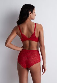 Soutien-gorge en dentelle rouge et culottes taille haute, avec des motifs floraux, des bretelles ajustables et des bords festonnés. Vue de dos affichée.