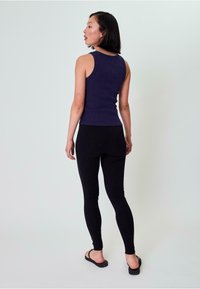 Granatowy prążkowany top na ramiączkach, dopasowany krój, w połączeniu z czarnymi legginsami, gładka faktura i płaskie czarne sandały. Widok z tyłu na jednolitym tle.