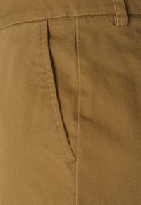 Pantalons en coton beige avec une texture lisse, coupe droite et poche latérale avec des détails de couture contrastants.
