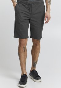 Shorts en coton gris avec taille élastique et cordon de serrage, dotés de poches latérales et d'une coupe décontractée, associés à des baskets noires.