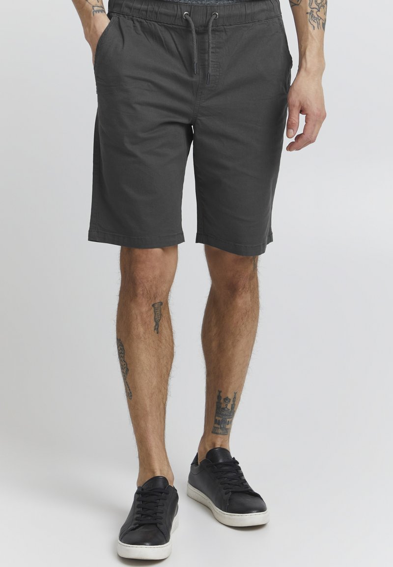 Shorts en coton gris avec taille élastique et cordon de serrage, dotés de poches latérales et d'une coupe décontractée, associés à des baskets noires.