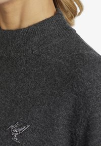 Ciemnoszary sweter z wysokim kołnierzem, wykonany z miękkiego materiału. Posiada małe haftowane logo kolibra na piersi.