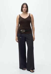 Top in maglia marrone con scollo a V, abbinato a pantaloni scuri grigi a gamba larga e vita alta, dotati di una cintura nera con fibbia dorata.