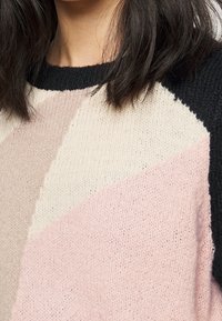 Strickpullover mit einem geometrischen Farbblockdesign in sanftem Rosa, Creme und Schwarz, runder Ausschnitt und strukturiertem Stoff.