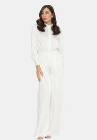 Blusa bianca a maniche lunghe con colletto, abbinata a pantaloni a gamba larga, caratterizzati da un motivo a pois discreto e una vestibilità sartoriale. Texture morbida.