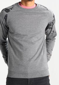 Sudadera gris con mangas raglán que presenta un sutil patrón floral negro. Fabricada en un tejido suave con puños y dobladillo acanalados.