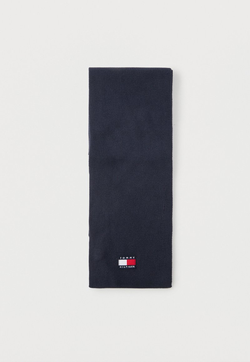 Διπλωμένο κασκόλ πλεκτό σε ναυτικό μπλε χρώμα με μικρό ορθογώνιο λογότυπο Tommy Hilfiger σε κόκκινο, λευκό και μπλε κοντά στην άκρη.