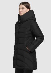 Svart puffjacka med hög krage, dragkedjestängning och sidofickor. Materialet är texturerat med ett quiltat mönster på sidorna.