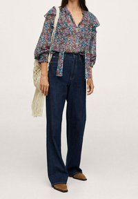 Blouse à imprimé floral avec manches à volants, associée à un jean en denim foncé taille haute. Accessoirisée d'un sac tissé et de bottines à talons marron.