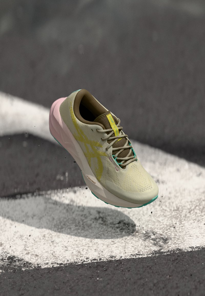Chaussure de course légère avec un upper en mesh beige, des accents jaunes et un talon rose. Dispose d'une semelle texturée et d'un branding prononcé.
