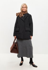Abrigo de plumas negro con cuello de chal y dos bolsillos frontales, combinado con una falda de punto gris, bolso marrón y bufanda de estampado de leopardo.