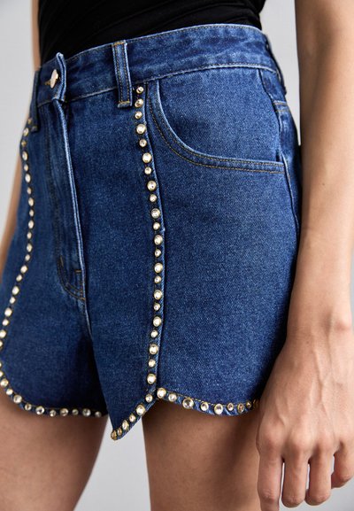 Shorts in denim blu con orlo scallop, adornati con dettagli in oro e trasparente lungo le cuciture laterali. Texture sfrangiata e taglio classico.