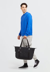 Borsa a duffel nera con maniglie doppie, chiusura con zip e tasca frontale. Realizzata in materiale resistente, presenta un logo e dettagli minimalisti.