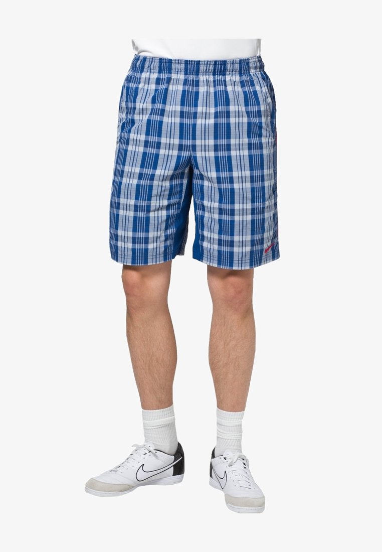 Blaue Karotten-Shorts mit einem elastischen Bund. Sie zeigen abwechselnd dunkle und helle blaue Karos. Getragen mit weißen Sneakers und Crew-Socken.