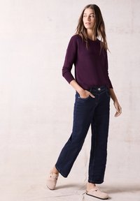 Lila Langarmoberteil, dunkelblaue weite Jeans und hellrosa Clogs mit einem Riemen. Einfaches Design ohne auffällige Muster oder Akzente.