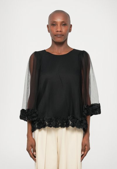 Blouse noire avec des manches en tulle transparent, col rond et dentelle florale en bordure. Texture douce et design fluide.