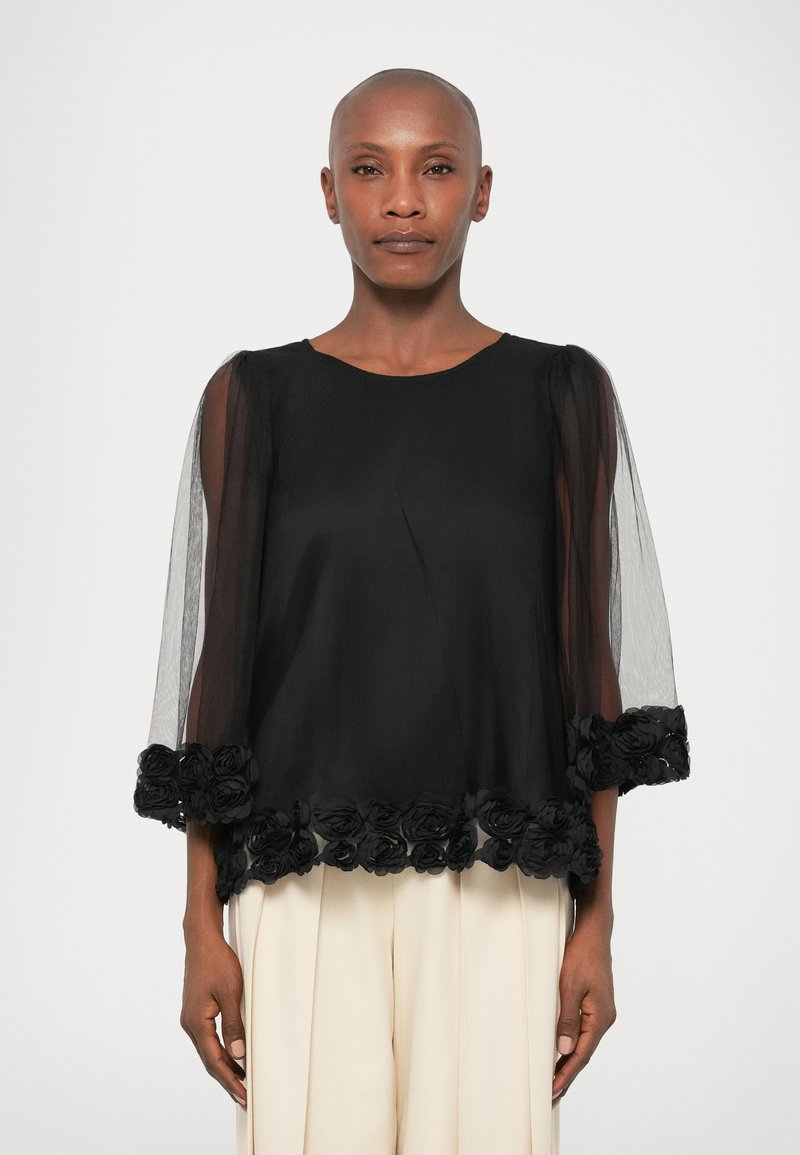 Black blouse with transparent tulle sleeves, round neck, and floral lace trim at the hem. Soft texture and flowy design.