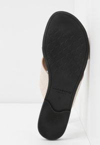 Sandale beige avec une tige texturée, un arrière ouvert, et une semelle en caoutchouc noire présentant un motif de bande de roulement en losange. Nom de la marque "VAGABOND" visible.