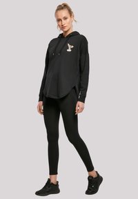 Svart hettegenser med frontlomme og sidelommer, prydet med et brodert design. Kombinert med svarte leggings og joggesko.