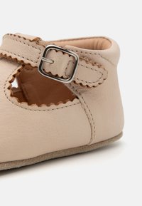 Beige skinnesko med utskårne detaljer, bølgete kanter og en sølvfarget spenne. Myk semsket såle for komfort.