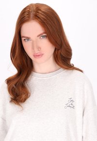 Lichtgrijze sweatshirt met een zachte textuur, voorzien van een ronde halslijn en korte mouwen, versierd met een marineblauwe geborduurde tekstdetail.