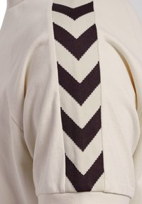 Lichtbeige sweatshirt met een gestructureerd donkerbruin en crèmekleurig zigzagpatroon aan de zijkant, met een zachte, gladde stofafwerking.