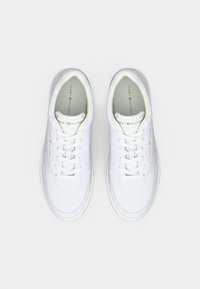 Ein Paar weiße Tommy Hilfiger Sneaker mit Schnürdesign, goldener Markenbezeichnung auf der Zunge und an den Seiten, von oben auf einem weißen Hintergrund betrachtet.