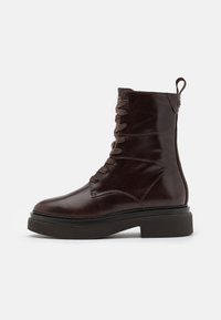 Brown leather ankle boot with lace-up front, rounded toe, chunky platform sole, and rear pull-tab. Smooth texture with subtle stitching details.