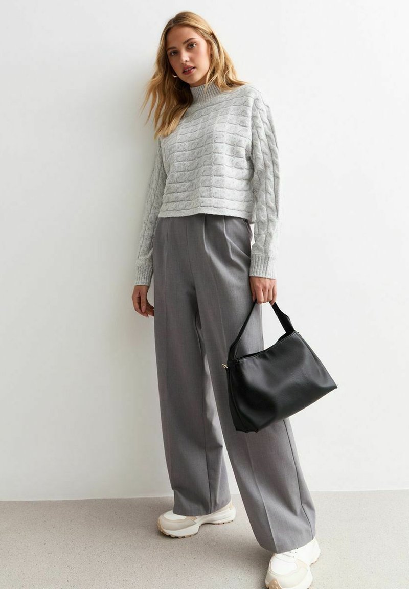 Maglione corto grigio a coste, pantaloni larghi plissettati grigi e una borsa a tracolla nera in pelle. Per completare il look, delle sneakers bianche con suola spessa.