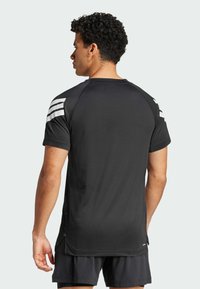 Camisa atlética negra con tejido texturizado, mangas cortas y acentos de rayas blancas en los hombros. Cuello redondo y aberturas laterales.