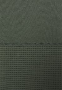 Dunkelgrüner Sportstoff mit einem glatten oberen Bereich und einem strukturierten unteren Bereich mit kleinen, erhabenen Rautenmuster.