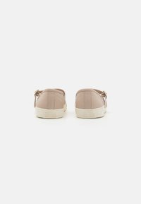 Zapatillas de color beige claro con parte superior de cuero suave, suelas de goma blanca y diseño con cordones. Incluye un detalle de hebilla lateral.
