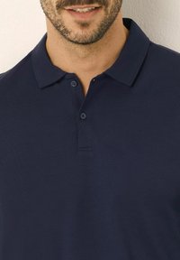 Marinblå polo-tshirt i bomull med krage, tvåknapprad och korta ärmar. Slät struktur utan mönster.