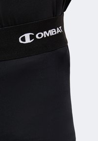 Gros plan sur une ceinture noire avec un texte blanc "COMBAT" et un logo stylisé "C" sur un vêtement de sport noir.