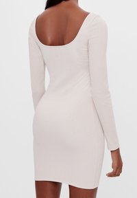 Langärmeliges, geripptes Kleid in hellem Beige mit einem U-Boot-Ausschnitt am Rücken und einer figurbetonten Silhouette, mit glatter Textur und knielangem Schnitt.