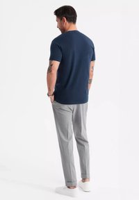 Maglietta a maniche corte blu navy abbinata a pantaloni grigi su misura, con vestibilità slim e risvolti; indossata con scarpe bianche slip-on.
