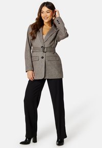 Blazer grigio a motivo houndstooth con vita con cintura, due tasche frontali e bottoni neri, abbinato a pantaloni neri a gamba larga e stivali con tacco.