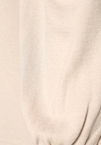 Beige neulekangas, sile pinta, jossa on hieno jousto, hienovarpunen kaarroskuvio ja lempeä laskostus. Ei näkyviä lisätietoja.