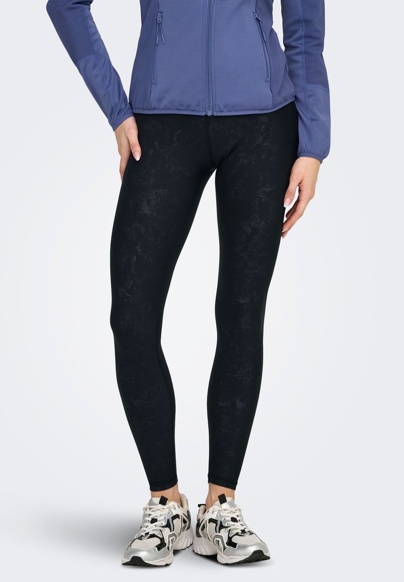 Black athletic leggings with a subtle textured pattern, paired with a blue jacket. Shoes are beige and black, with a chunky design.