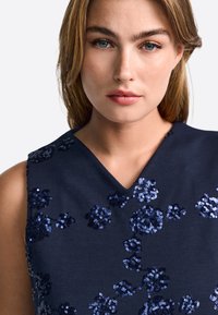 Tmavomodrý tielkový top s výstrihom do V, zdobený kvetinovými vzormi z tmavomodrých flitrov na textúrovanom materiáli.